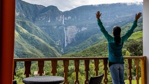 A person on a balcony with a view of a mountainous landscape and a waterfall. - Gocta Andes Lodge (Cocachimba)