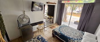 Una habitación con cama, escritorio, silla, televisor y ventana con cortinas.
