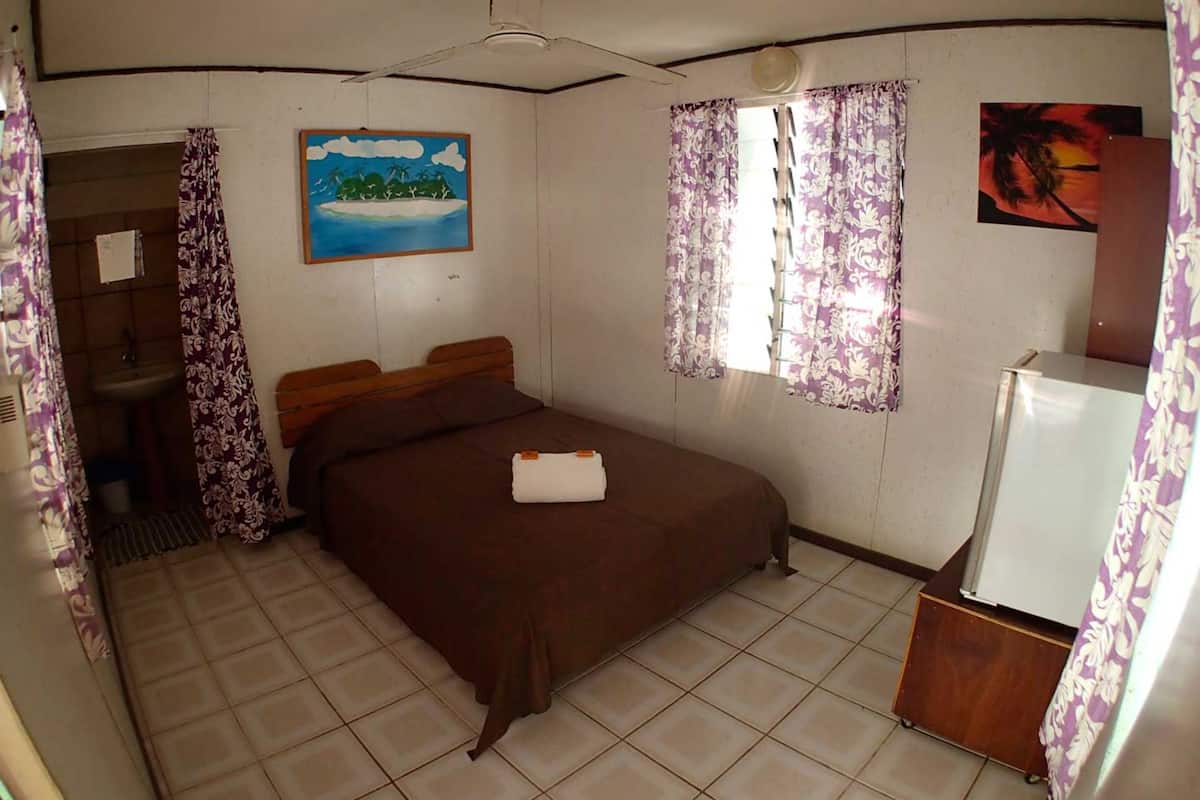 A bedroom with a bed, a shower, a painting, and a refrigerator.