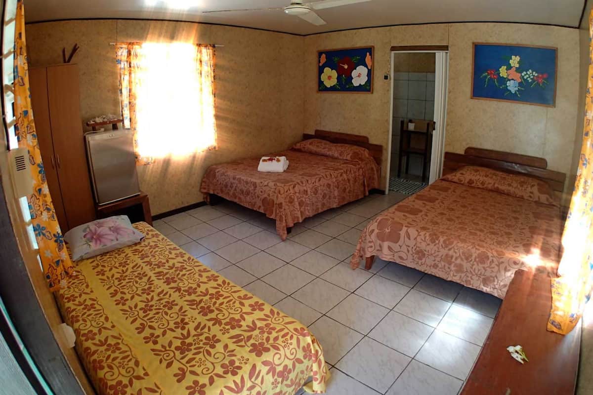 A hotel room with three beds, a refrigerator, a wardrobe, and two floral paintings.