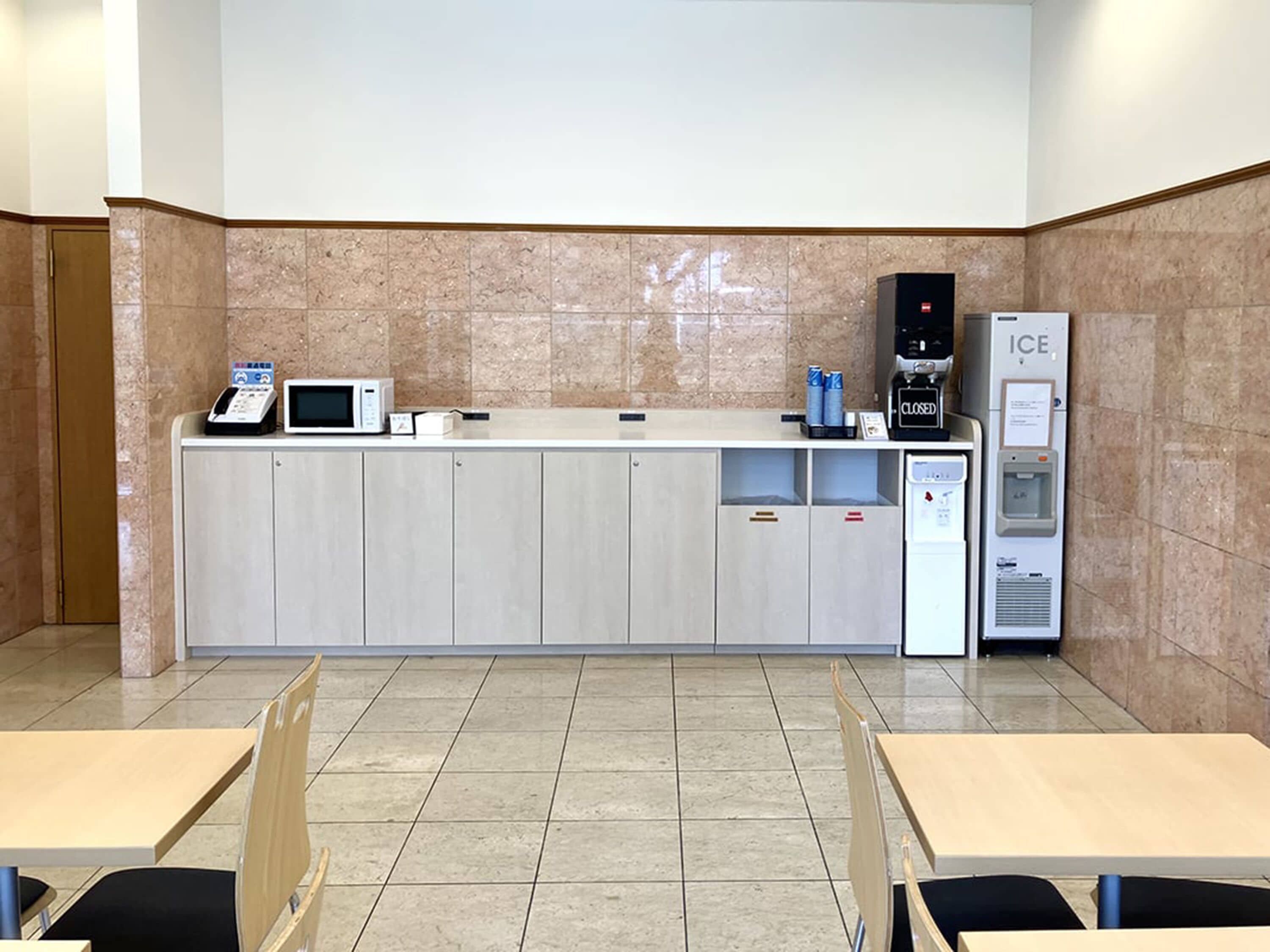 Een keurig, modern keukenhoekje met een magnetron, koffieapparaat en een ijsmachine. Er zijn kastjes en een waterkoeler.