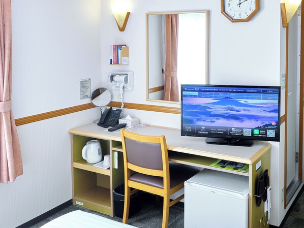 Habitación de hotel con escritorio, silla, computadora, teléfono, espejo y un refrigerador pequeño.