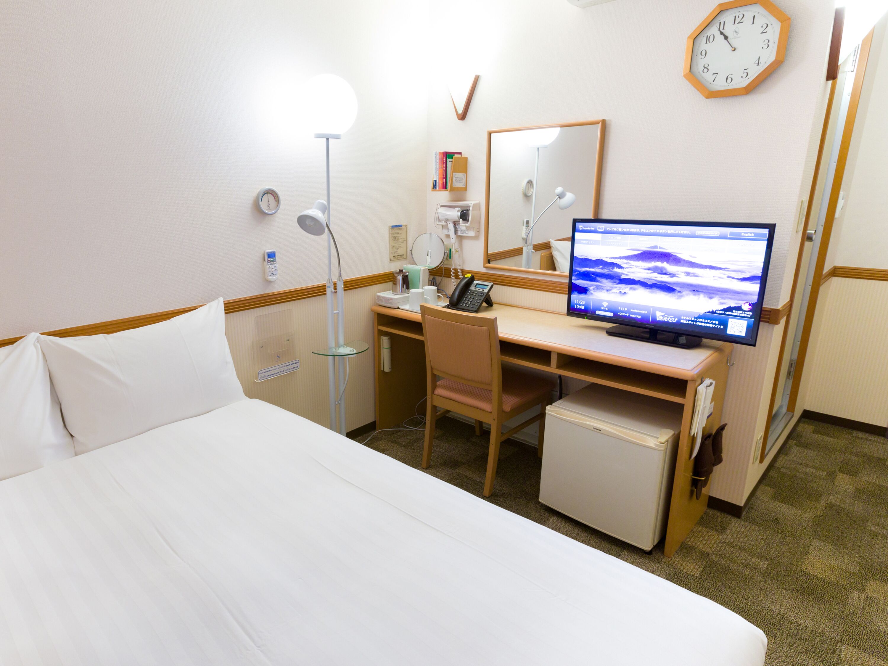 A hotel room with a bed, desk, chair, and a small refrigerator.