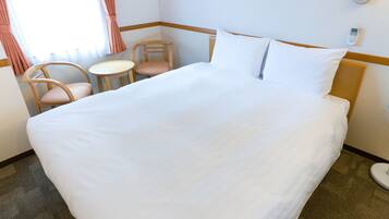 A hotel room with a large bed, two chairs, a small table, and a thermostat on the wall.