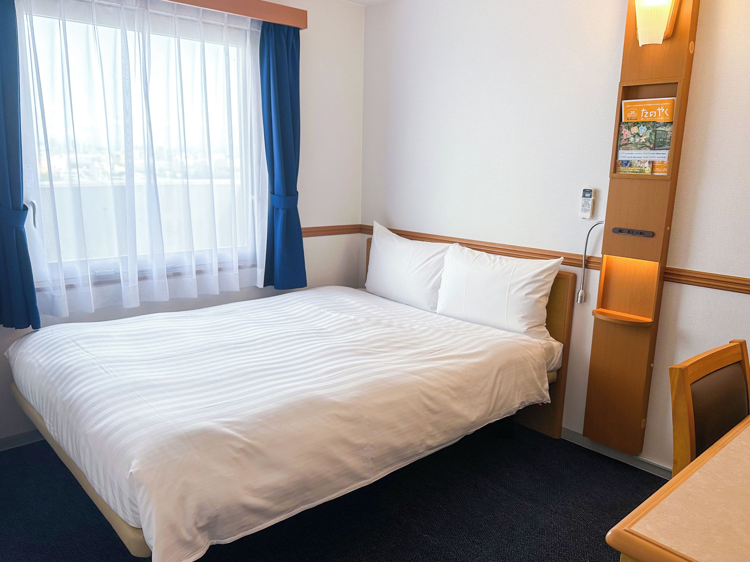 A hotel room with a bed, a bedside table, a lamp, and a window with curtains.