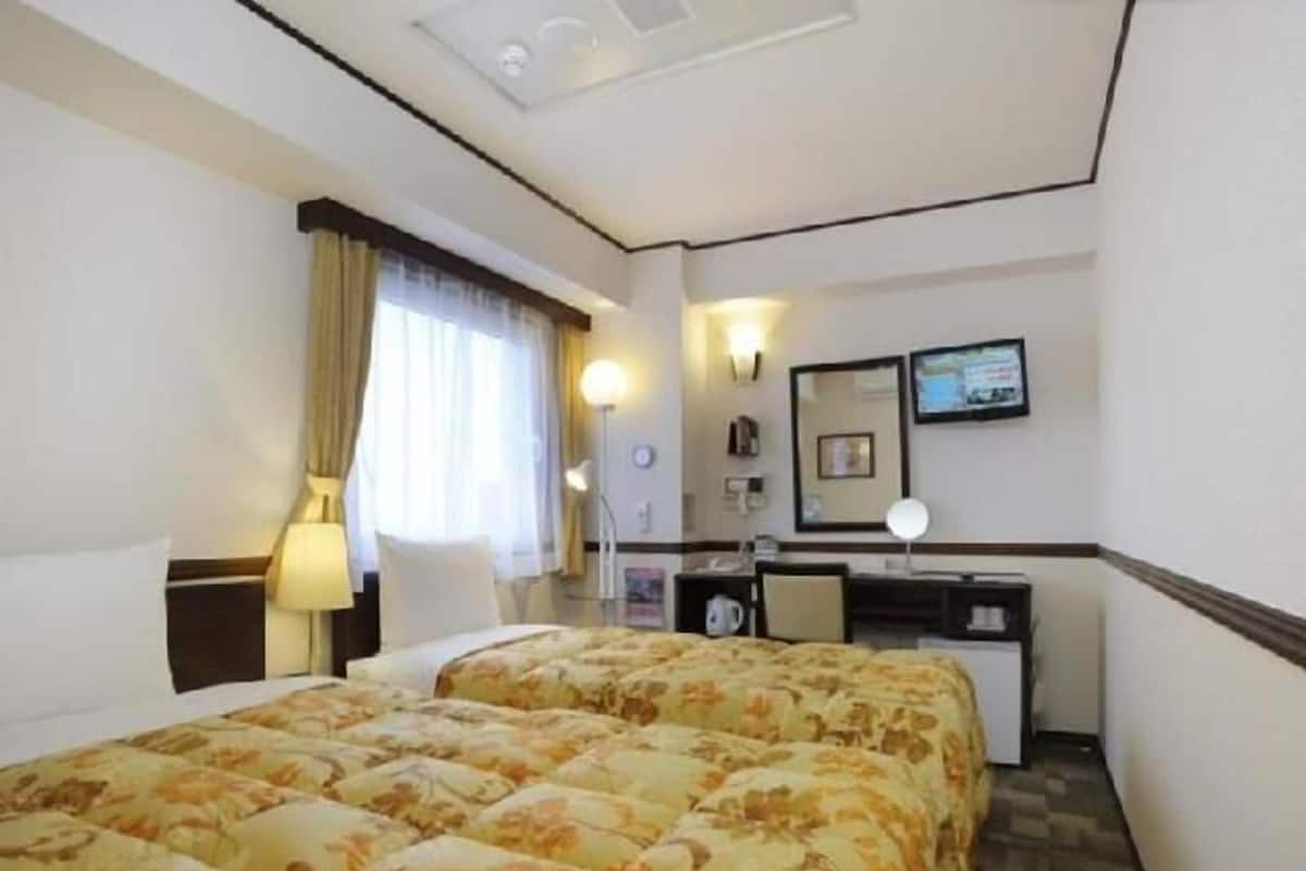 A hotel room with two beds, a desk, a chair, a lamp, a TV, and a window with curtains.