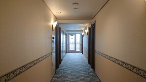 A hotel hallway with a patterned carpet, light-colored walls, and a door at the end leading to a balcony. - Toyoko Inn Hanshin Amagasaki Ekimae (Amagasaki)