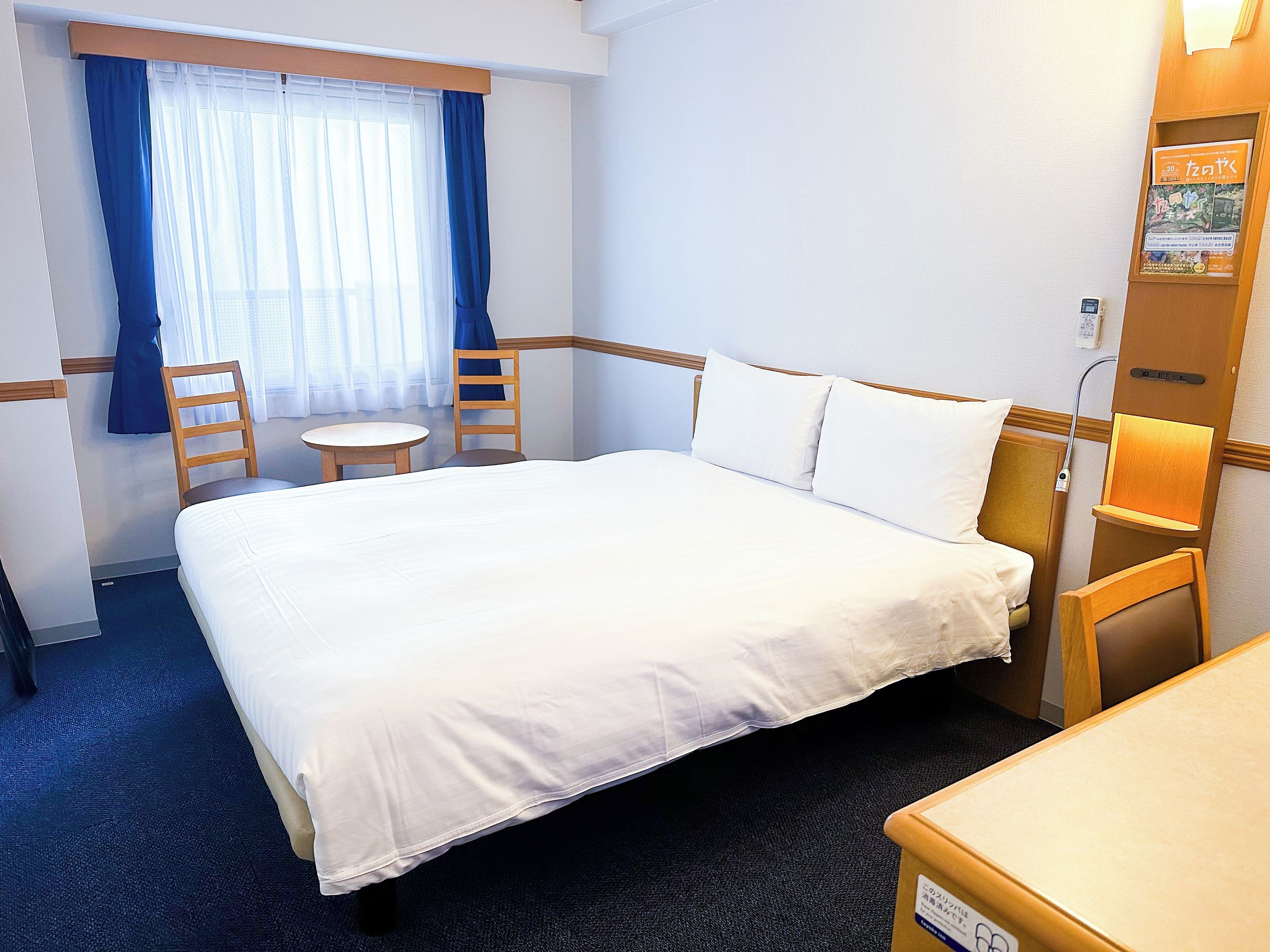 A hotel room with a bed, a chair, a small table, and a window with curtains.