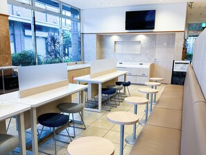 A modern cafe with high tables, chairs, and a seating area with round tables and benches. - Toyoko Inn Hanshin Amagasaki Ekimae (Amagasaki)