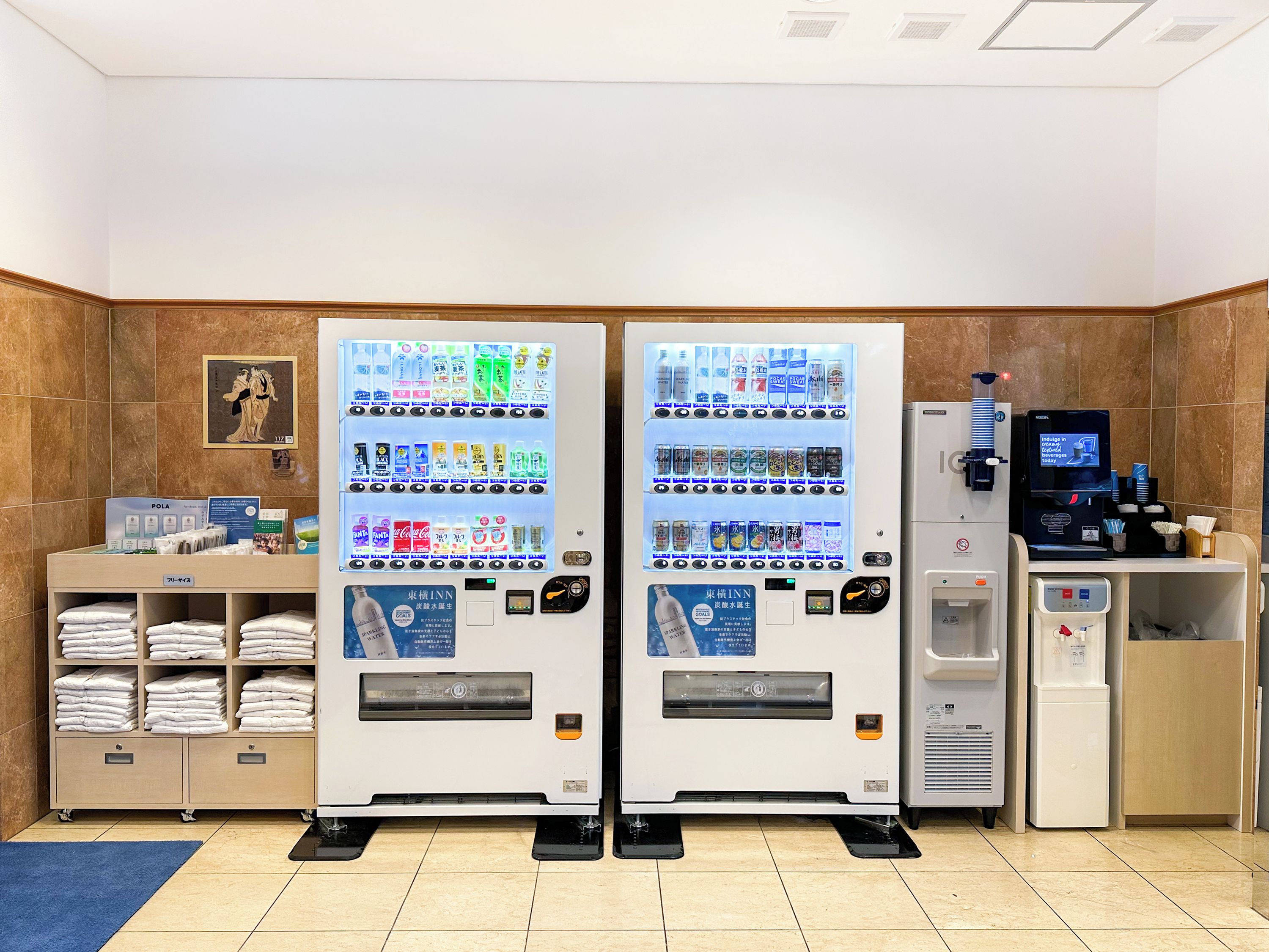 Et hotel lobby med to automater, en vanddispenser og et område med håndklæder.