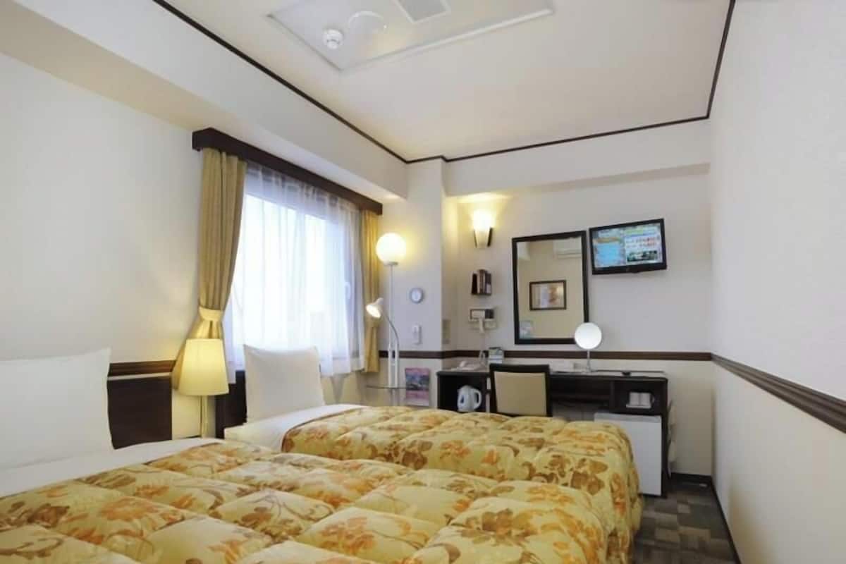 A hotel room with two beds, a desk, a chair, a desk lamp, a mirror, and a television.