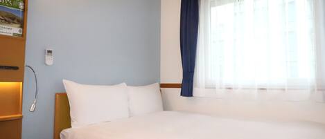 A hotel room with a bed, a bedside table, a lamp, a window with curtains, and a wall-mounted phone.