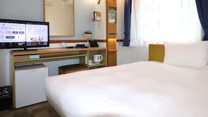 Quarto de hotel com cama, escrivaninha com computador, pequena geladeira, cafeteira e janela com cortinas.
