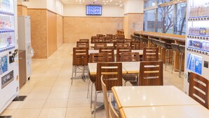 Cafeteria com mesas, cadeiras, máquinas de venda automática e uma tela digital exibindo uma oferta de 5% de desconto.