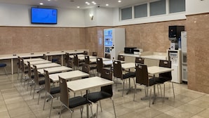 Uma sala de conferência com mesas, cadeiras, uma máquina de vendas automática, um micro-ondas e um frigorífico.