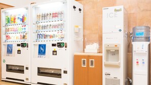 Máquinas de venda automática com bebidas e snacks, um dispensador de água e um armário com suporte para toalhas.