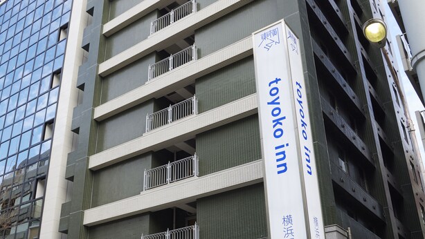 Um edifício com a placa da Toyoko Inn. Possui vários andares com varandas e um design arquitetônico moderno.
