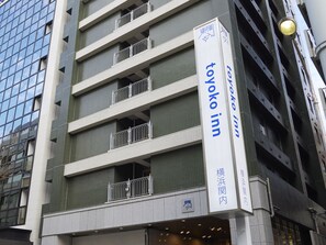 Een gebouw met een bord voor Toyoko Inn. Het heeft meerdere verdiepingen met balkons en een modern architectonisch ontwerp.