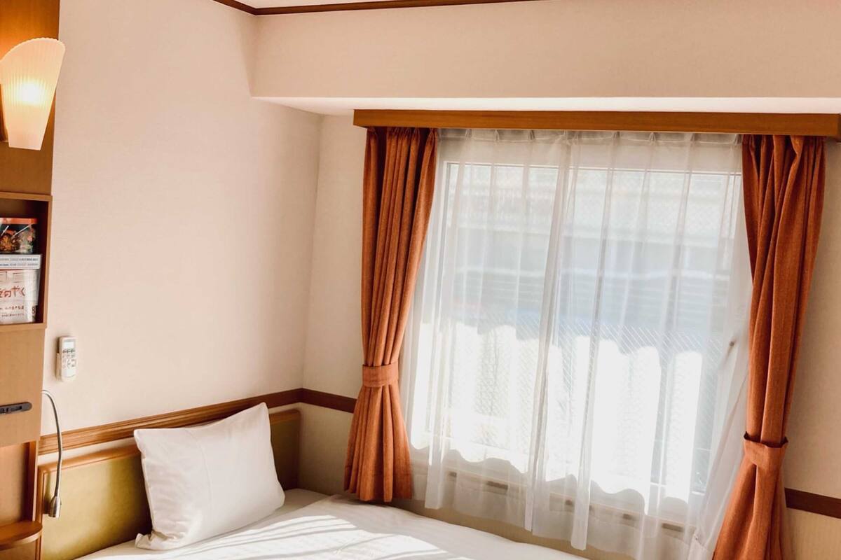 A hotel room with a bed, a nightstand, a lamp, and a window with curtains.