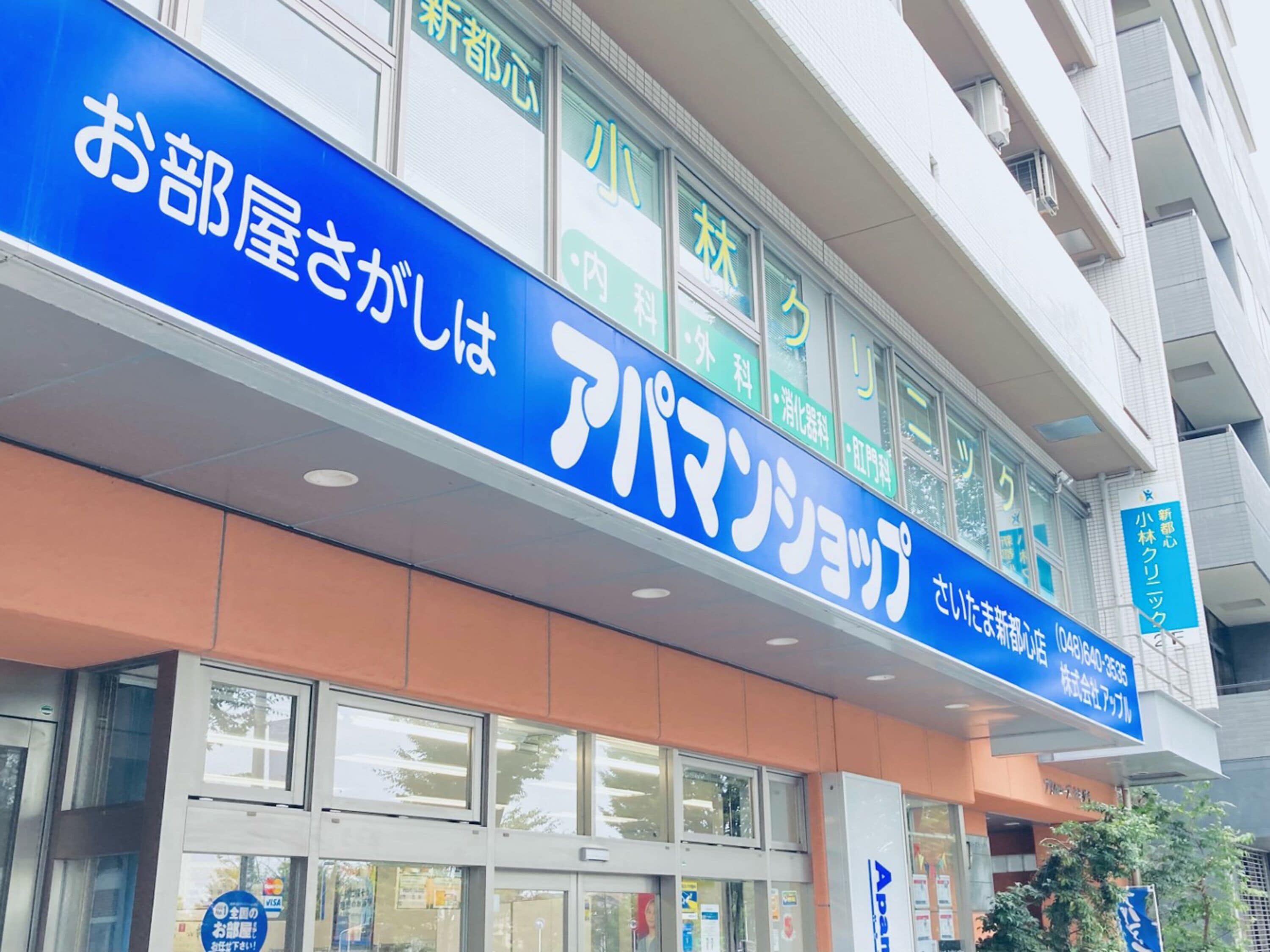 Un edifici amb un cartell blau que diu “お部屋さがし” i “アパマンション”. 