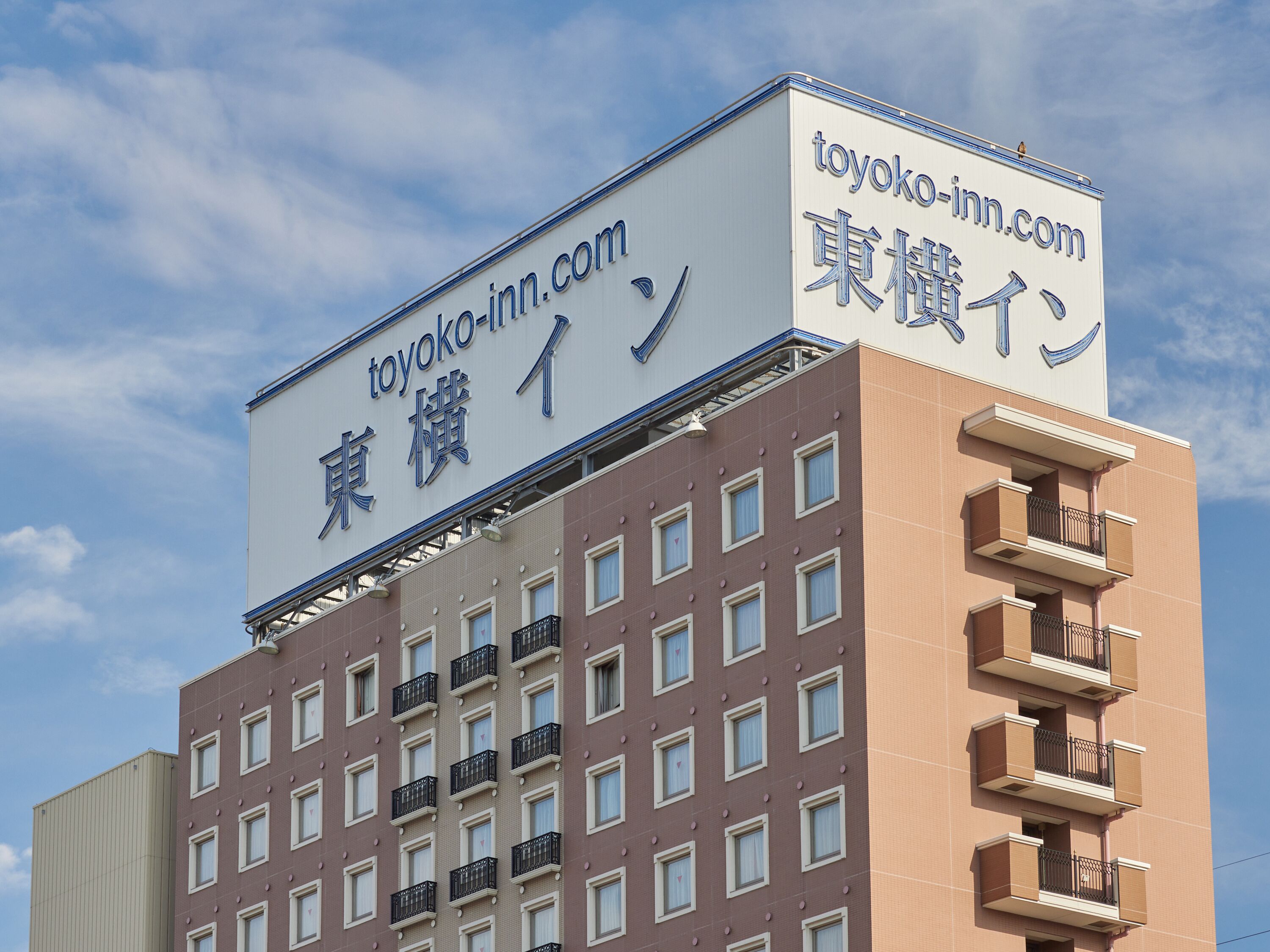 Un bâtiment sur lequel on peut lire une enseigne avec l’inscription « toyoko-inn.com » et des caractères japonais.