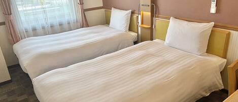 A hotel room with two single beds, a window with curtains, a thermostat, and a bedside table.