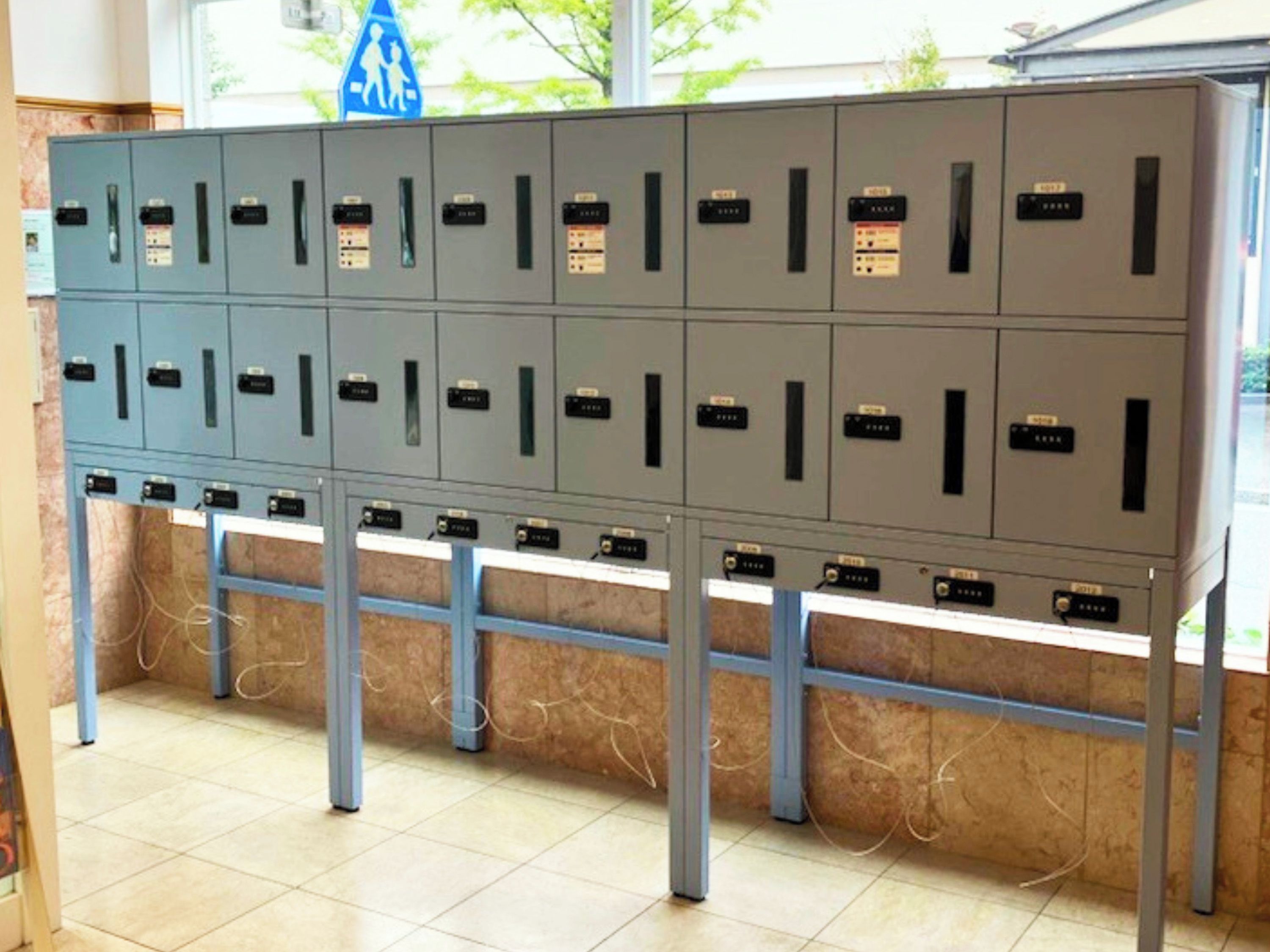 A row of metal storage lockers with labels, standing on a tiled floor.