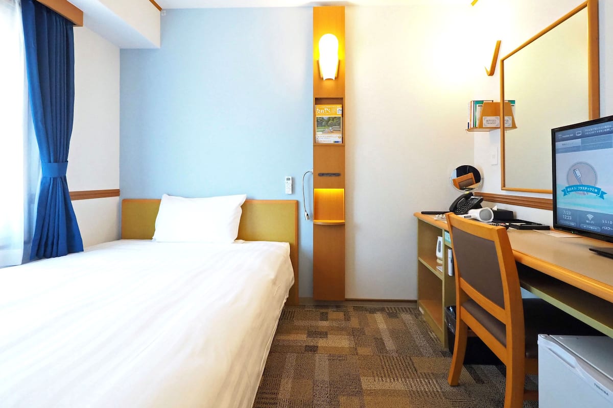A hotel room with a bed, desk, computer, and a mirror.
