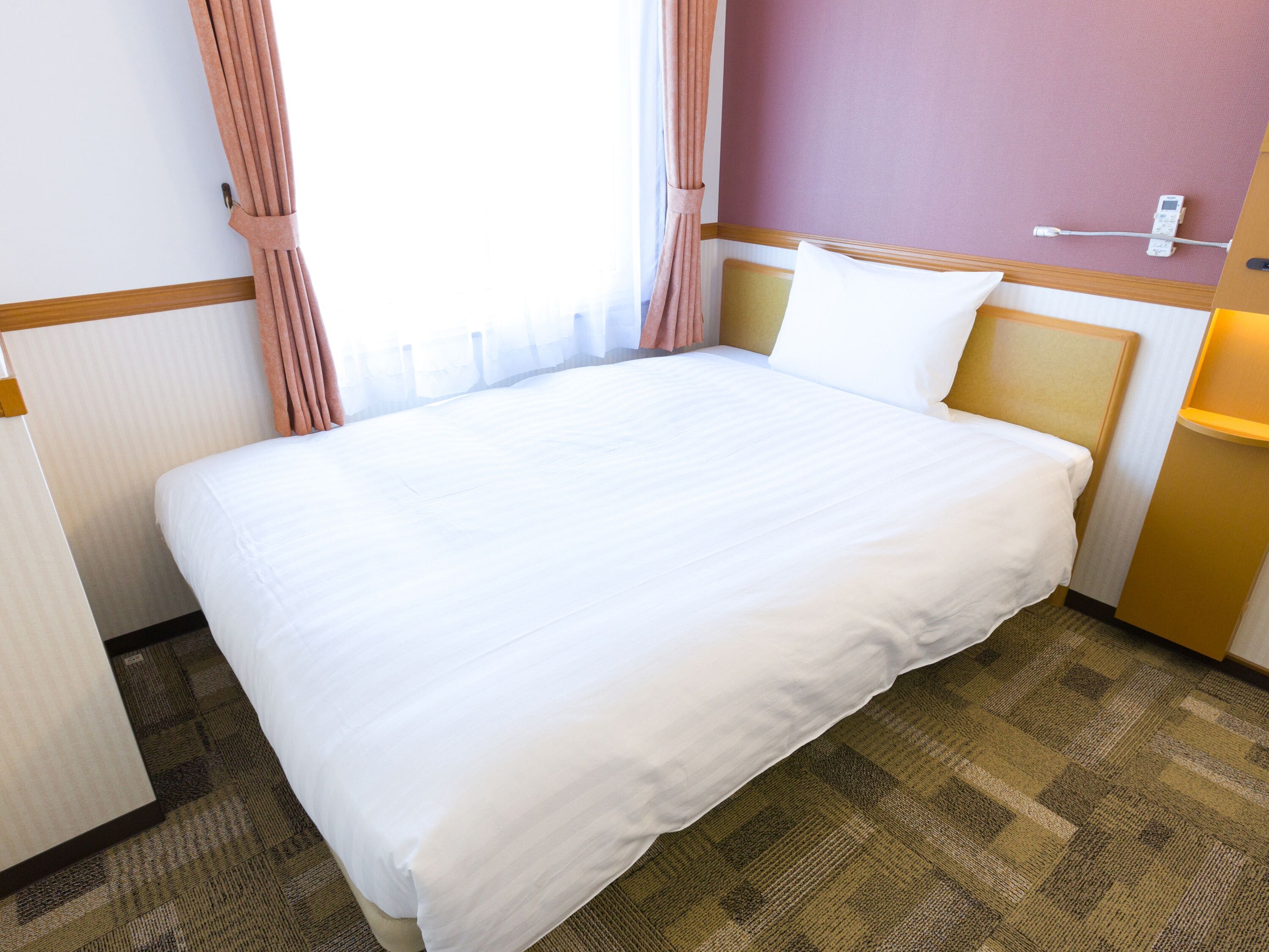 A hotel room with a large bed, a bedside table, a lamp, and a window with curtains.
