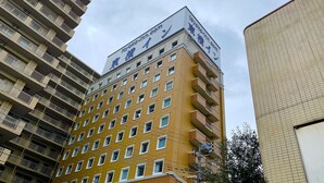 Ein mehrgeschossiges Hotel mit einem gut sichtbaren Schild für 'tavoko-inn.com' auf dem Dach. Das Gebäude hat eine gelbe Fassade mit mehreren Balkonen und Fenstern.