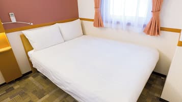 Quarto de hotel com cama bem arrumada, abajur, telefone e janela com cortinas.