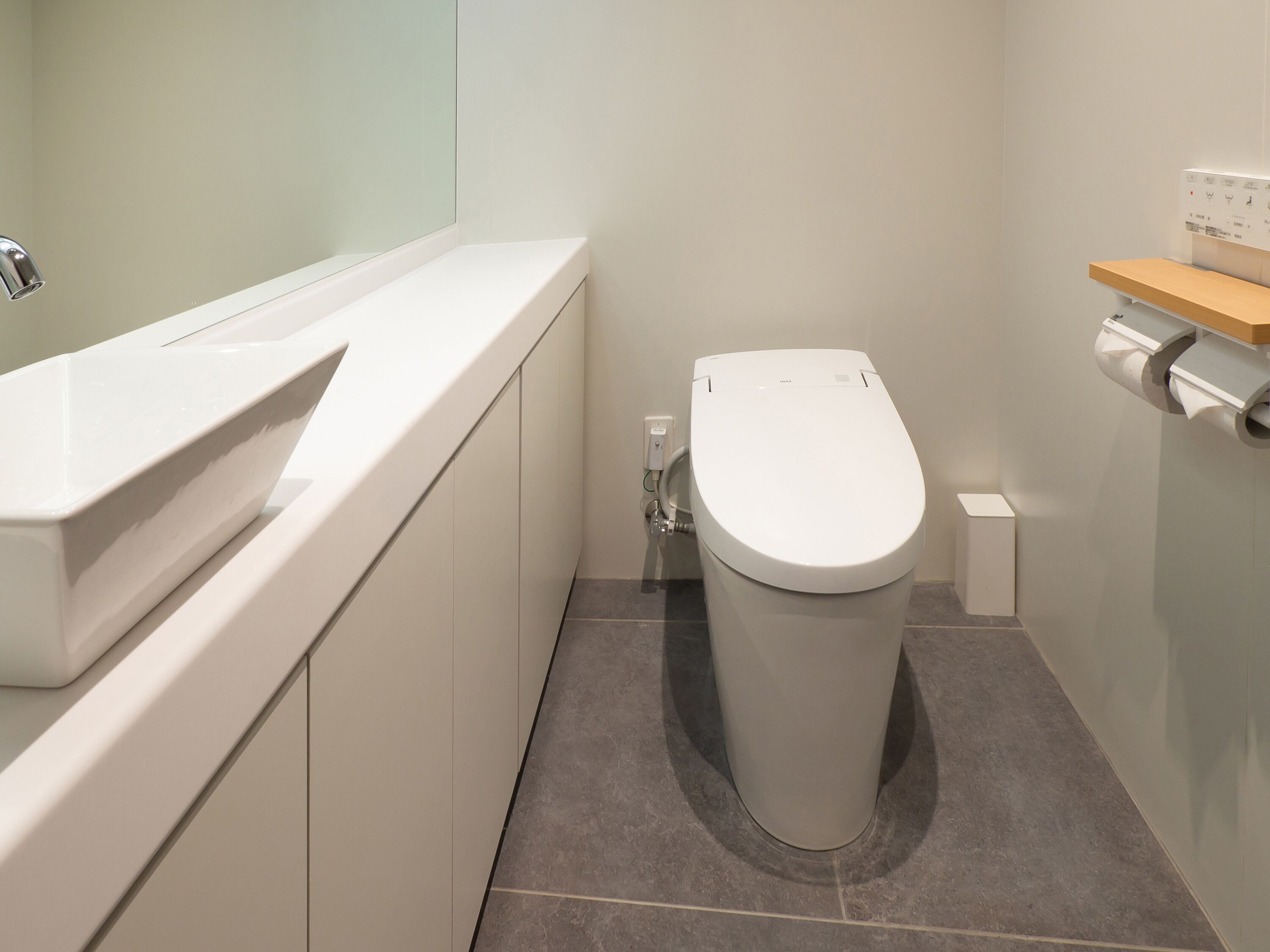 Un baño moderno con un inodoro blanco, un lavabo blanco y un pequeño estante de madera.