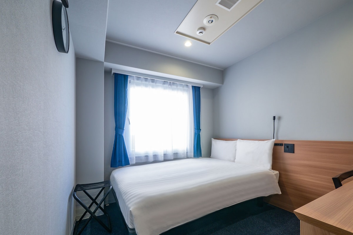 Habitación de hotel con cama, escritorio, ventana con cortinas e iluminación en el techo.