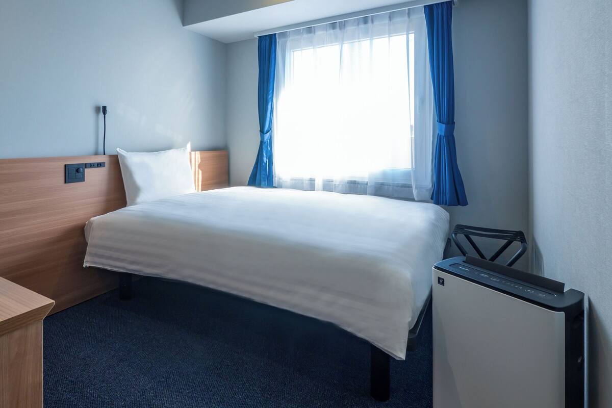 Una habitación de hotel con una cama, un escritorio, una silla, una mesita y una ventana con cortinas.