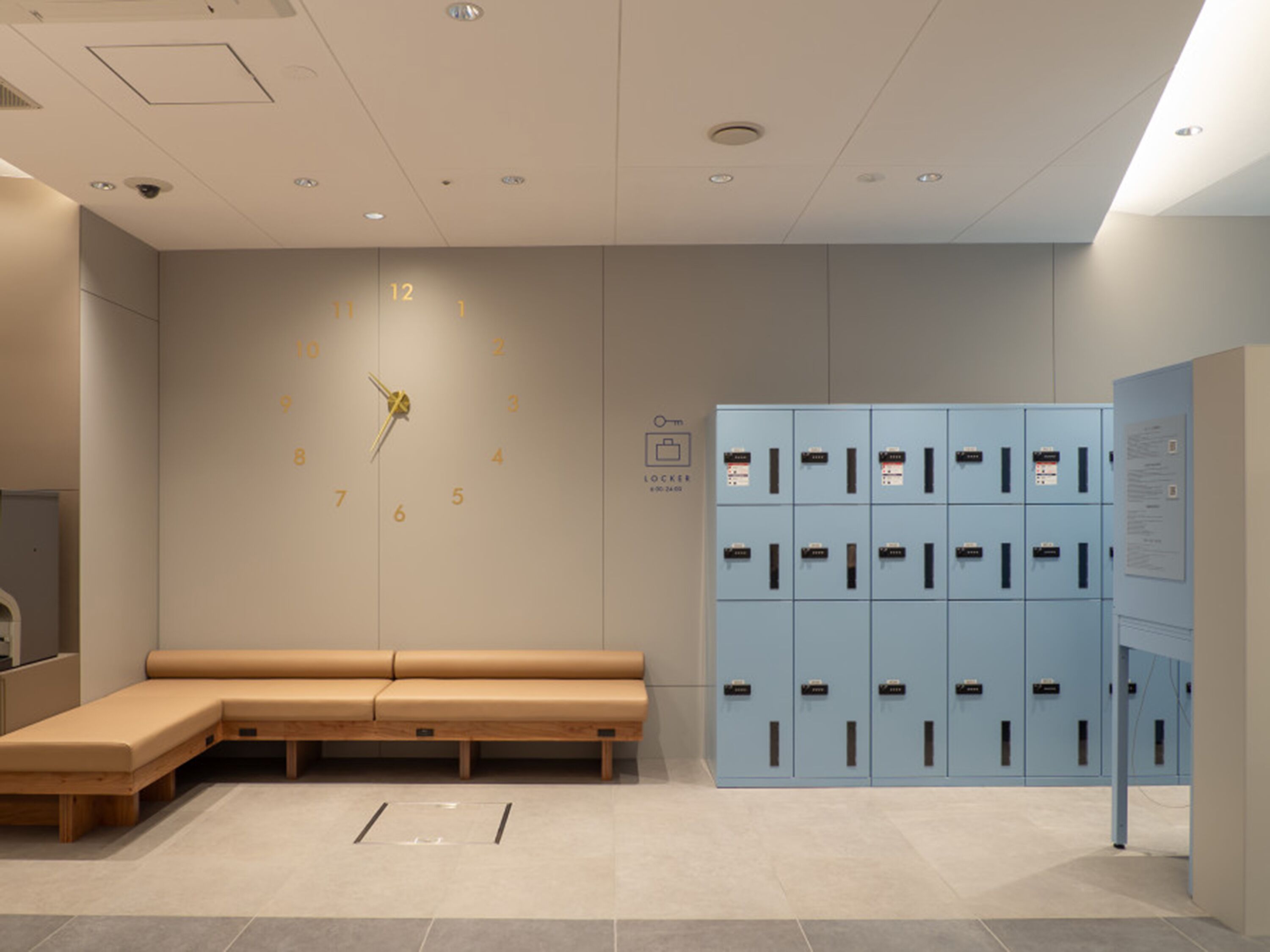 A modern waiting area with a bench, a wall clock, and a row of lockers.