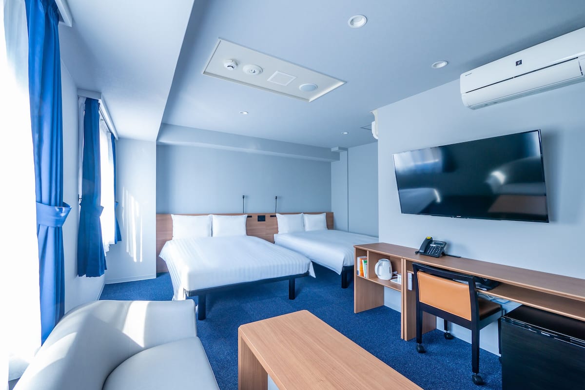 Habitación de hotel con dos camas, un escritorio, una silla, un televisor y un equipo de aire acondicionado.