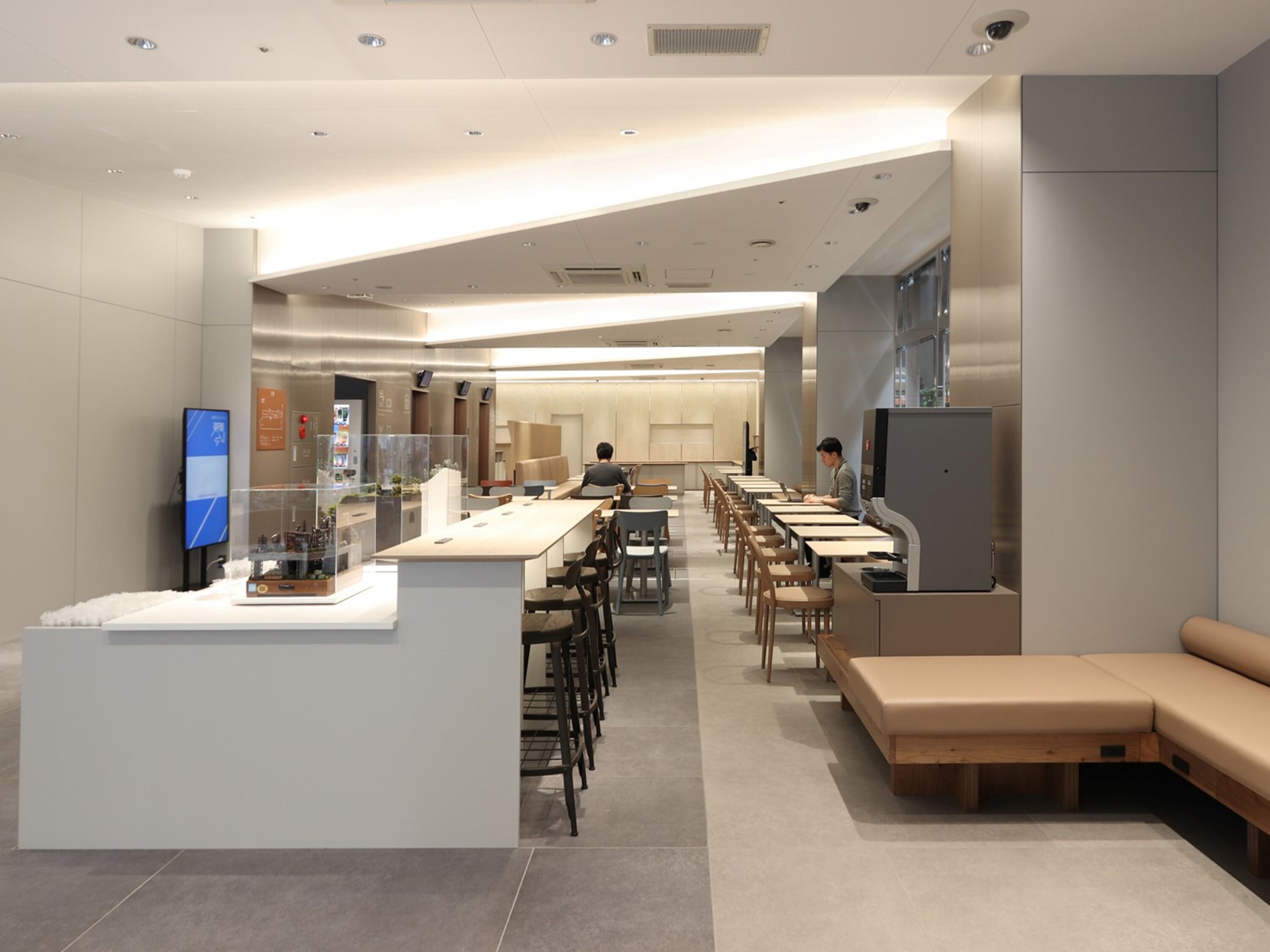 Un restaurante moderno y espacioso con largas mesas, cabinas, una barra con mostrador y una pantalla grande a la izquierda.