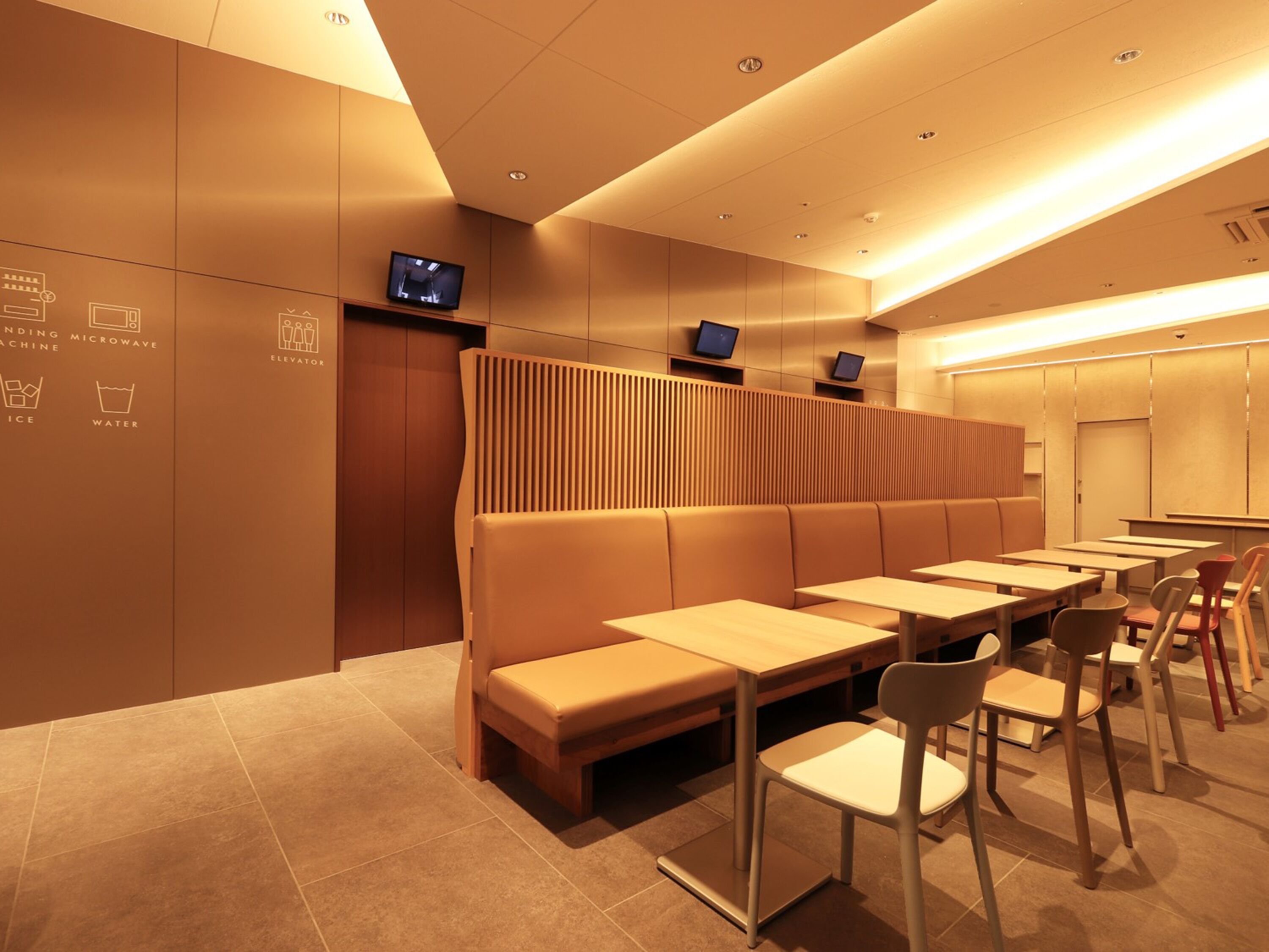A modern restaurant with booths and tables, a counter, and a television screen.