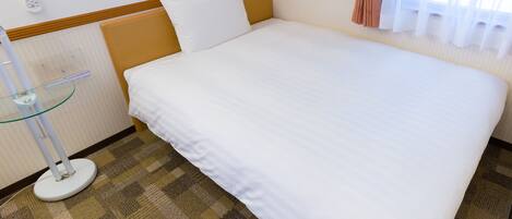 Habitación de hotel con cama, mesita de noche con lámpara, control remoto y ventana con cortinas.