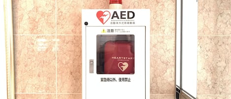 Un desfibrilador automático externo (DEA) montado en la pared, con una señal de advertencia e instrucciones en inglés y japonés.