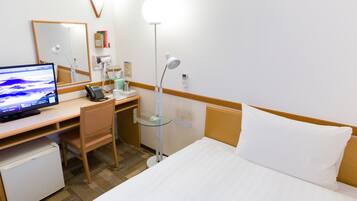 Habitación de hotel con cama, escritorio con computadora, silla, refrigerador pequeño, mesita de noche, lámpara y espejo.
