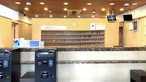 A reception area with a 'FRONT' sign, a counter with a computer monitor, a security camera, and a row of vending machines.