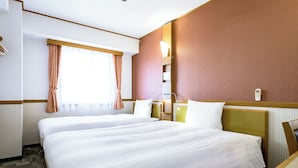A hotel room with two beds, a window with curtains, a bedside table, and a wall-mounted phone.