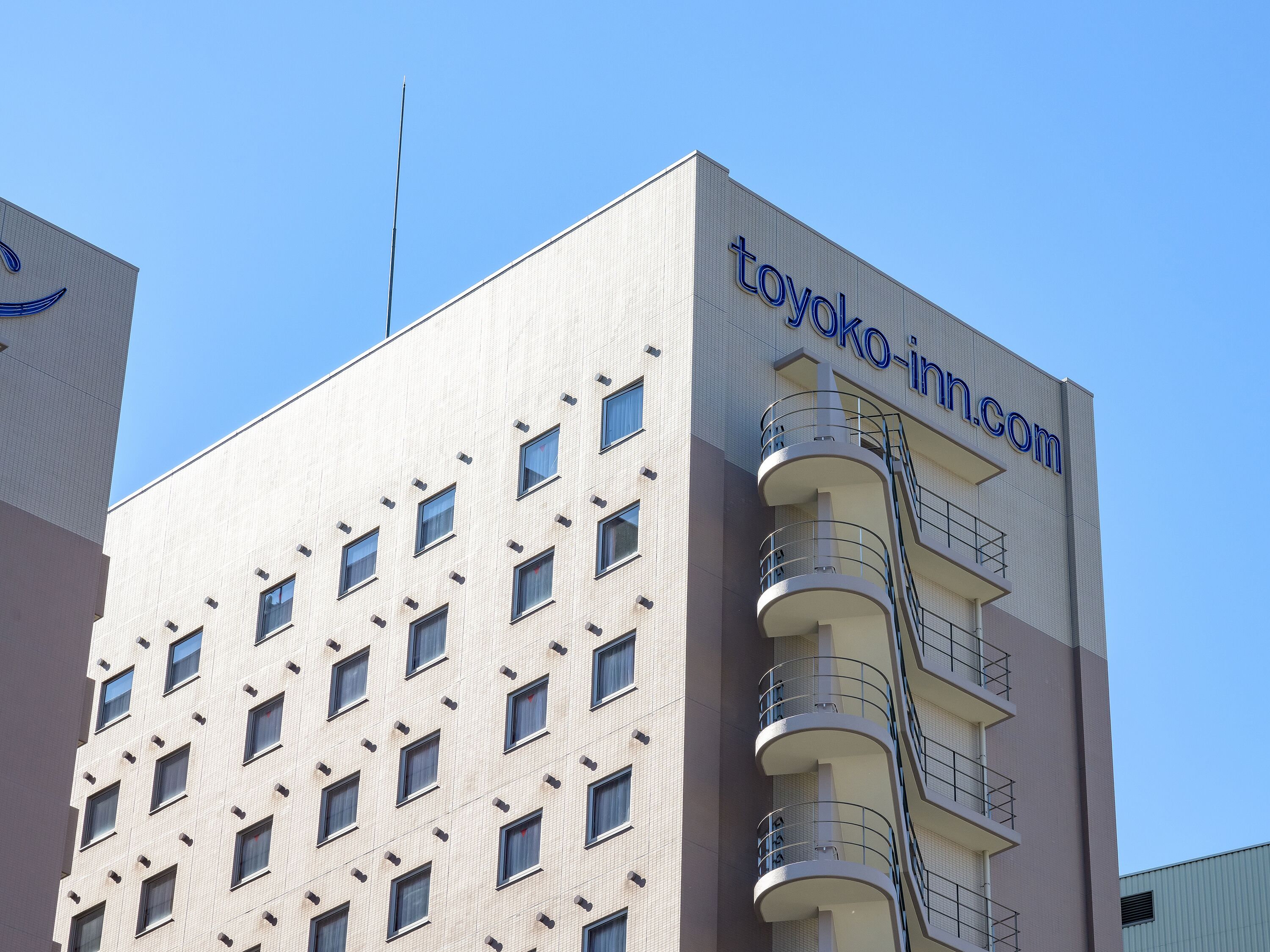 A modern building with a flat facade, multiple windows, and a prominent sign reading "toyoko-in.com".