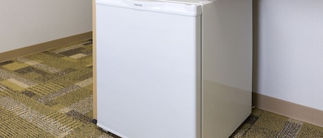A compact white refrigerator in a corner of a room with a patterned carpet.