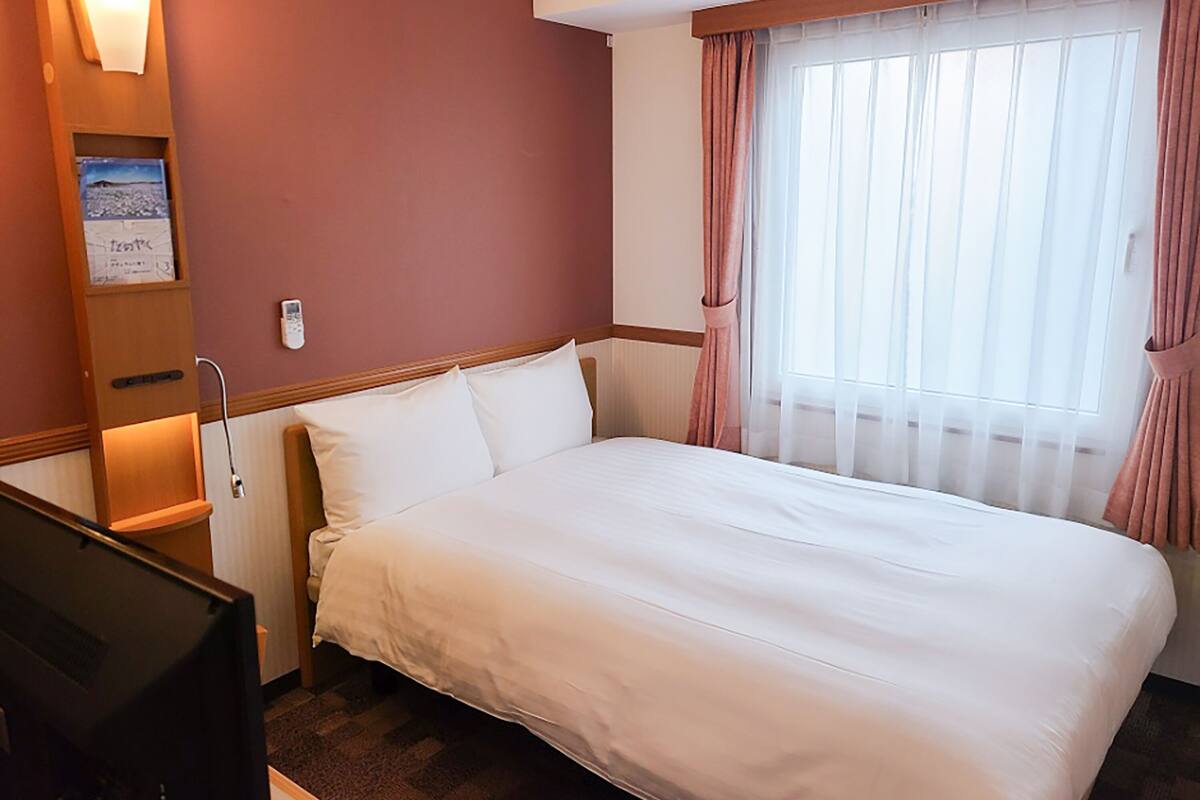 Une chambre d’hôtel avec un grand lit, une table de chevet, une télévision et une fenêtre avec des rideaux.