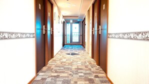A hotel hallway with patterned carpet, wooden doors, and a view of the outside through a glass door at the end. - Toyoko Inn Nagoya Owari Ichinomiya Ekimae (Ichinomiya)
