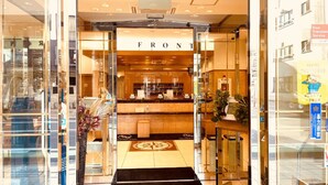 A hotel entrance with a reception desk, a sign reading "FRONT", and a small plant on the right. - Toyoko Inn Nagoya Owari Ichinomiya Ekimae (Ichinomiya)