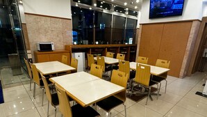 A modern dining area with multiple tables and chairs, a refrigerator, and a television mounted on the wall.