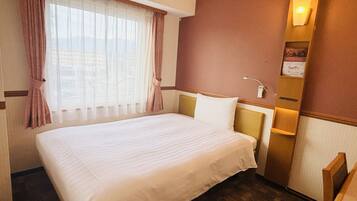 A hotel room with a large bed, a window with curtains, a wall-mounted light, and a small table with a lamp.